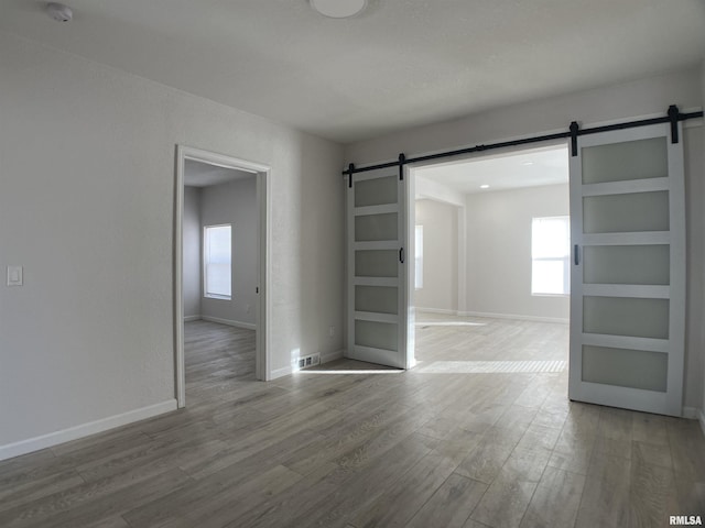 spare room with wood-type flooring, a healthy amount of sunlight, and a barn door