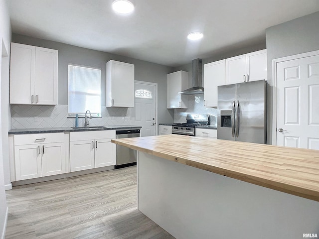 kitchen with wall chimney exhaust hood, wood counters, white cabinets, appliances with stainless steel finishes, and sink