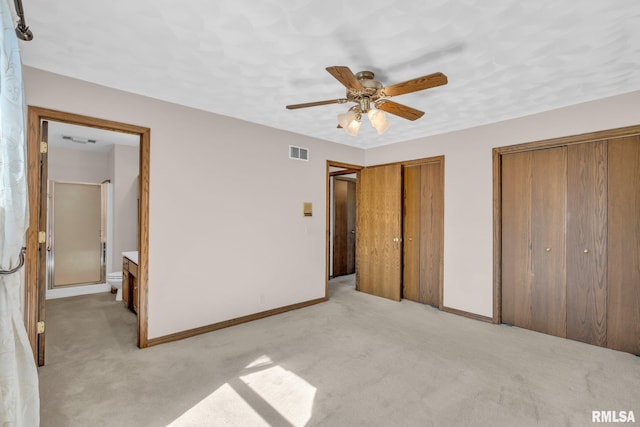 unfurnished bedroom with ensuite bathroom, ceiling fan, light colored carpet, and two closets