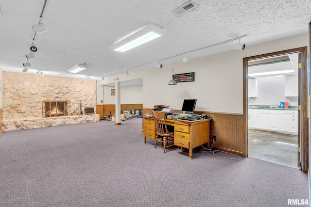 home office featuring carpet flooring, wood walls, a fireplace, and a textured ceiling