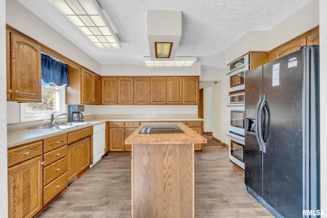 kitchen featuring black appliances, a center island, light wood-type flooring, and sink