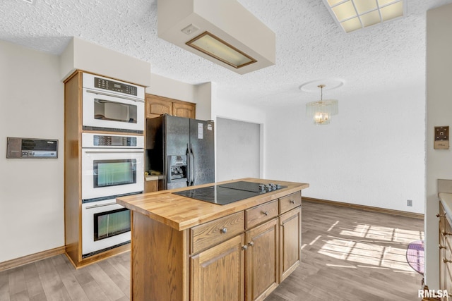 kitchen featuring black appliances, light hardwood / wood-style floors, hanging light fixtures, and wooden counters