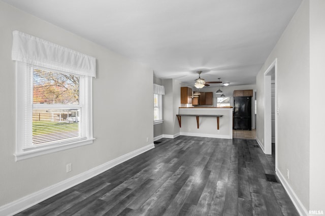 unfurnished living room featuring dark wood-type flooring and ceiling fan