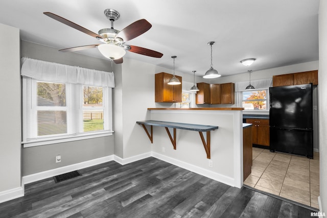 kitchen featuring dark hardwood / wood-style floors, black refrigerator, plenty of natural light, and kitchen peninsula