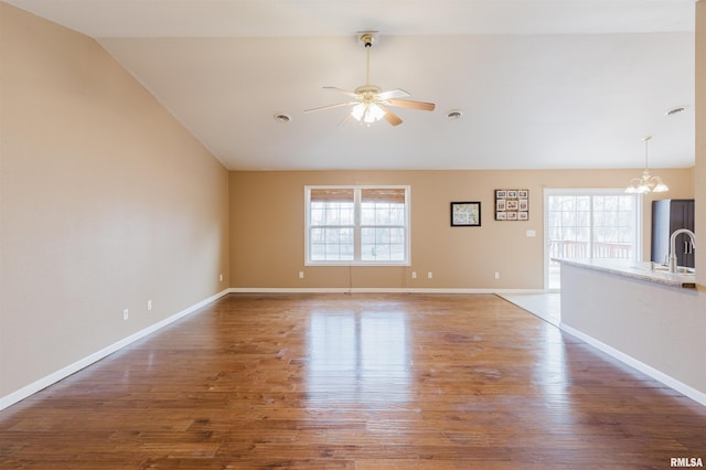 unfurnished living room featuring hardwood / wood-style floors, ceiling fan with notable chandelier, vaulted ceiling, and plenty of natural light