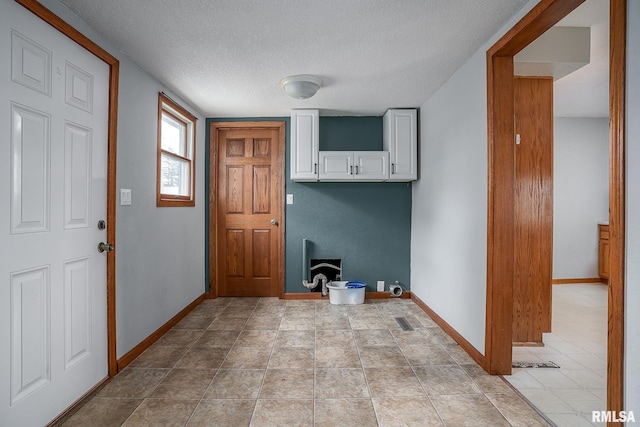 laundry area featuring light tile patterned flooring, cabinets, and a textured ceiling