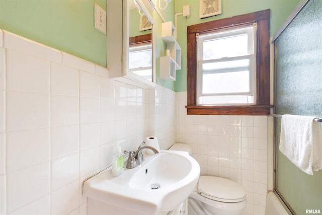 full bathroom with tile walls, enclosed tub / shower combo, sink, and toilet