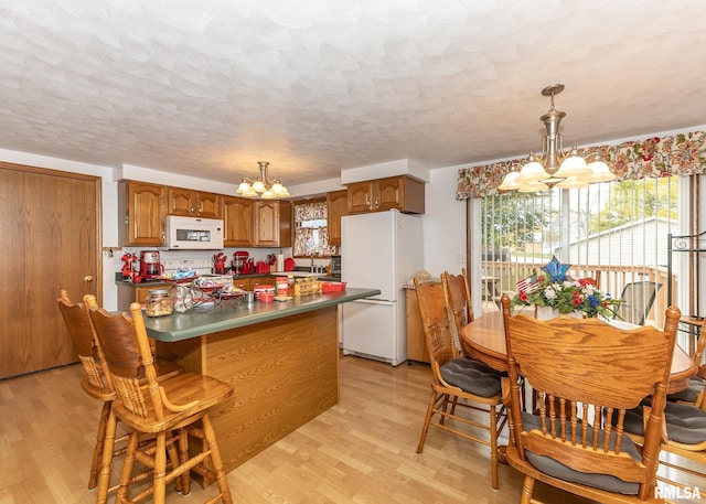 kitchen with a textured ceiling, white appliances, decorative light fixtures, an inviting chandelier, and light hardwood / wood-style floors