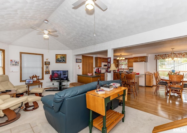 living room featuring ceiling fan with notable chandelier, light hardwood / wood-style floors, and vaulted ceiling