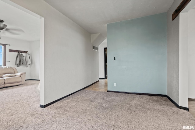 carpeted empty room featuring a barn door and ceiling fan