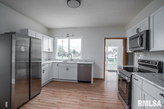 kitchen featuring tasteful backsplash, stainless steel appliances, sink, light hardwood / wood-style flooring, and white cabinets