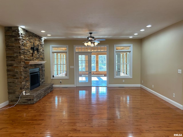 unfurnished living room featuring hardwood / wood-style flooring, ceiling fan, and a stone fireplace