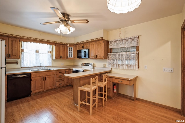 kitchen featuring sink, kitchen peninsula, a kitchen bar, black appliances, and light wood-type flooring