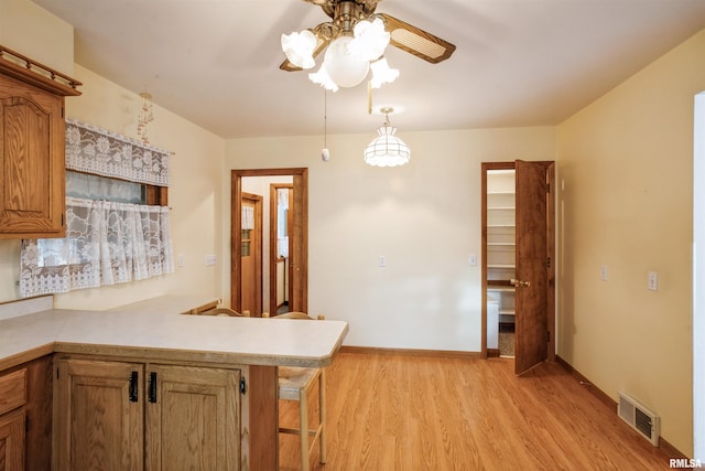 kitchen featuring kitchen peninsula, a breakfast bar, ceiling fan, light hardwood / wood-style floors, and hanging light fixtures