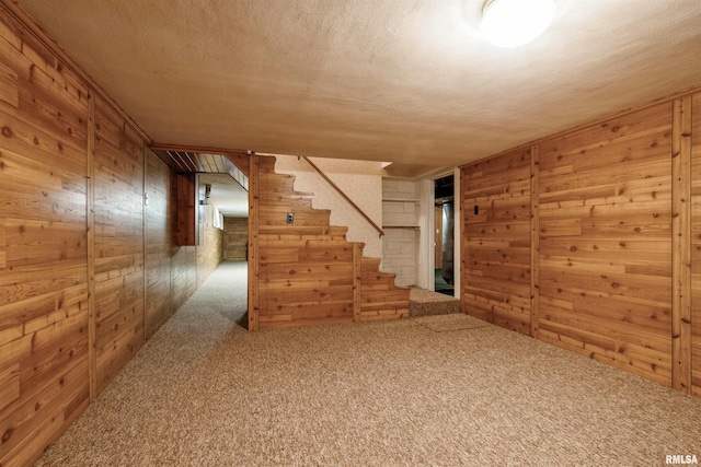 interior space with a textured ceiling, carpet floors, and wood walls