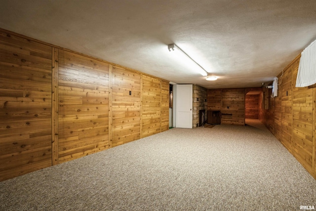 basement featuring carpet, a textured ceiling, and wood walls