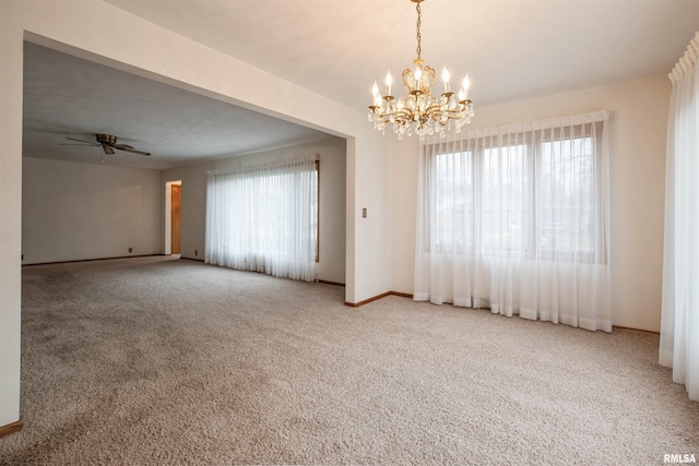 carpeted spare room featuring plenty of natural light and ceiling fan with notable chandelier