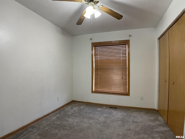 unfurnished bedroom featuring ceiling fan, a closet, a textured ceiling, and dark colored carpet