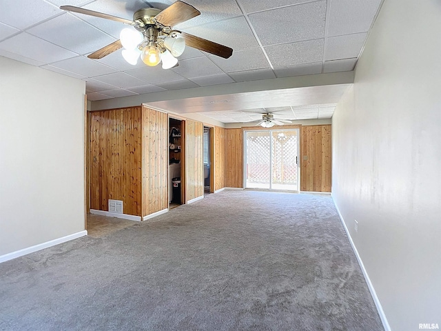 carpeted empty room featuring a paneled ceiling, wood walls, and ceiling fan