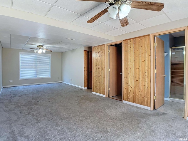 unfurnished room with wood walls, a drop ceiling, carpet, and ceiling fan