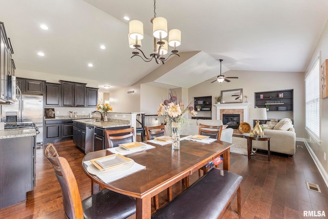 dining space featuring ceiling fan with notable chandelier, sink, dark wood-type flooring, and vaulted ceiling