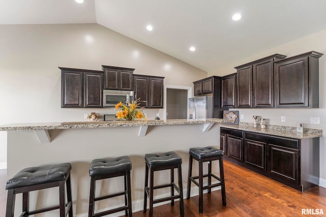 kitchen with dark hardwood / wood-style flooring, vaulted ceiling, a kitchen bar, a kitchen island, and appliances with stainless steel finishes