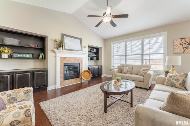 living room featuring built in shelves, vaulted ceiling, ceiling fan, dark wood-type flooring, and a tile fireplace