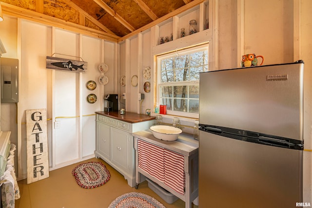 kitchen featuring white cabinetry, sink, electric panel, stainless steel fridge, and lofted ceiling