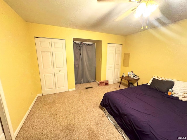 carpeted bedroom with a textured ceiling, ceiling fan, and multiple closets