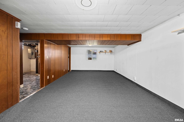 basement featuring dark colored carpet, wood walls, and electric panel