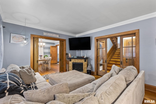 living room featuring a fireplace, wood-type flooring, crown molding, and a notable chandelier