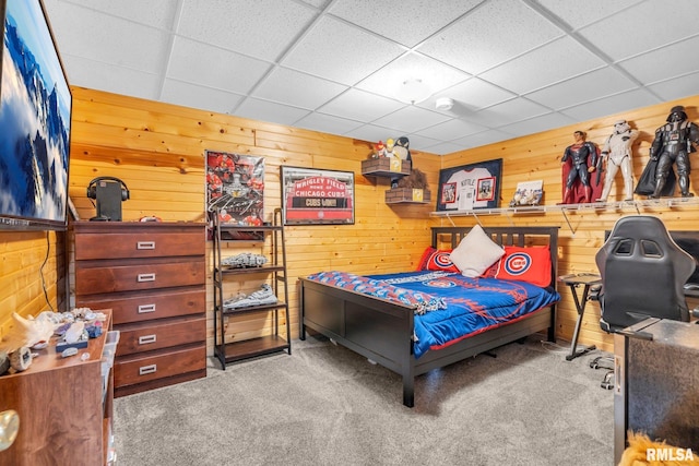 bedroom with a paneled ceiling, wood walls, and carpet