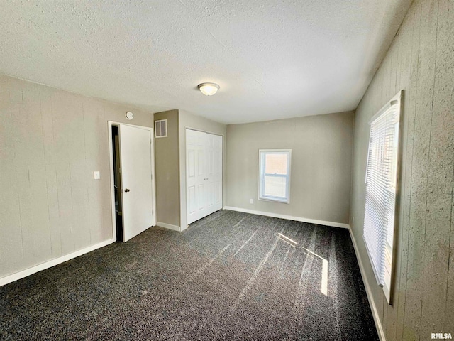 unfurnished bedroom with a closet, a textured ceiling, and dark colored carpet