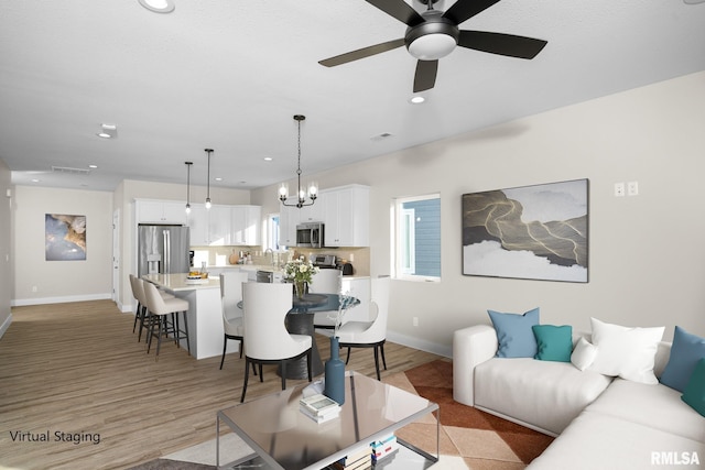 living room with ceiling fan with notable chandelier and light hardwood / wood-style flooring