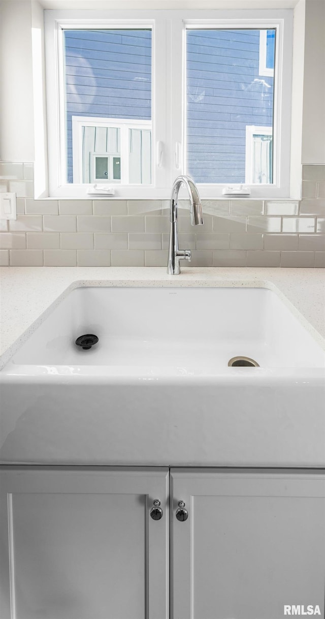 interior details with white cabinetry, light stone countertops, and tasteful backsplash