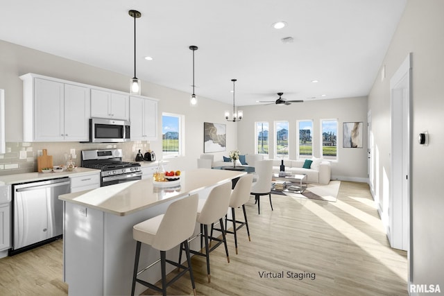 kitchen with pendant lighting, light wood-type flooring, appliances with stainless steel finishes, a kitchen island, and white cabinetry