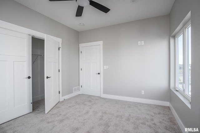 unfurnished bedroom featuring multiple windows, a closet, light colored carpet, and ceiling fan