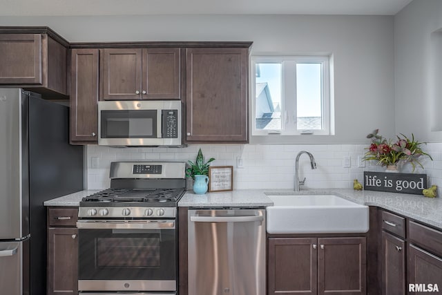 kitchen featuring dark brown cabinets, stainless steel appliances, light stone counters, and sink