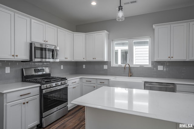 kitchen featuring sink, dark wood-type flooring, decorative light fixtures, white cabinets, and appliances with stainless steel finishes