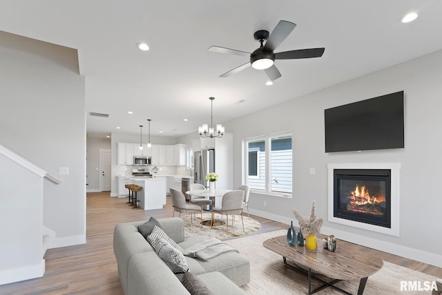 living room featuring ceiling fan with notable chandelier and light hardwood / wood-style floors