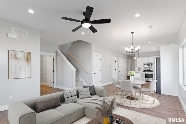 living room with ceiling fan with notable chandelier and light hardwood / wood-style floors