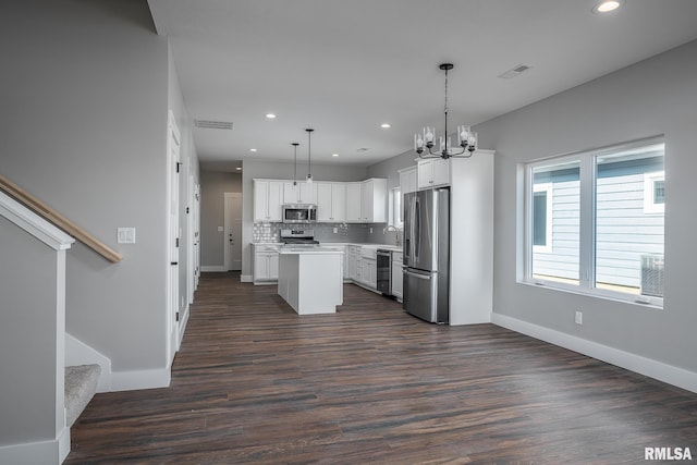 kitchen featuring appliances with stainless steel finishes, dark wood-type flooring, decorative light fixtures, a center island, and white cabinetry