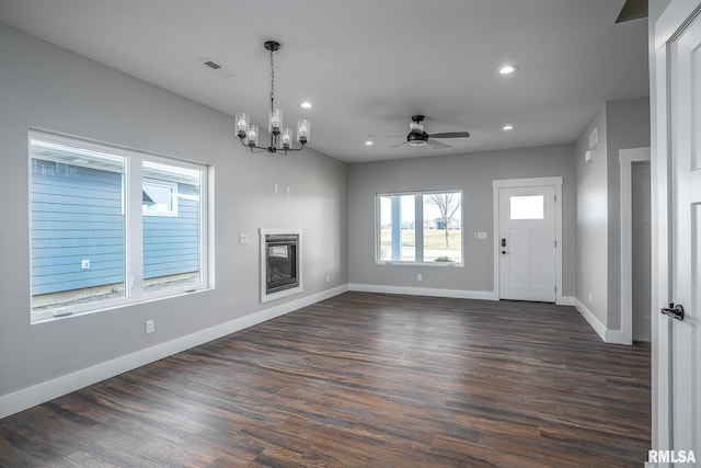 unfurnished living room with ceiling fan with notable chandelier and dark hardwood / wood-style flooring