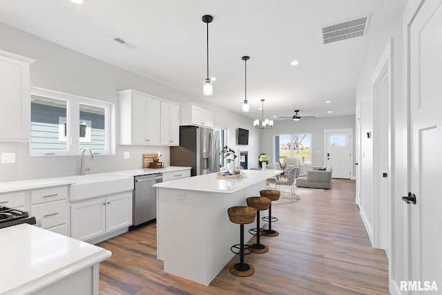 kitchen featuring a kitchen island, dark hardwood / wood-style floors, white cabinets, ceiling fan with notable chandelier, and appliances with stainless steel finishes