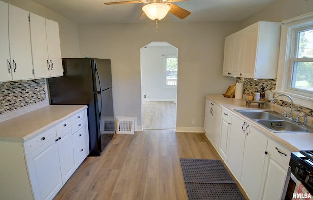 kitchen with black refrigerator, sink, decorative backsplash, light wood-type flooring, and white cabinetry