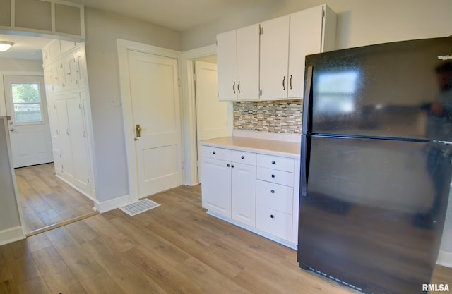 kitchen featuring decorative backsplash, black refrigerator, white cabinets, and light hardwood / wood-style flooring