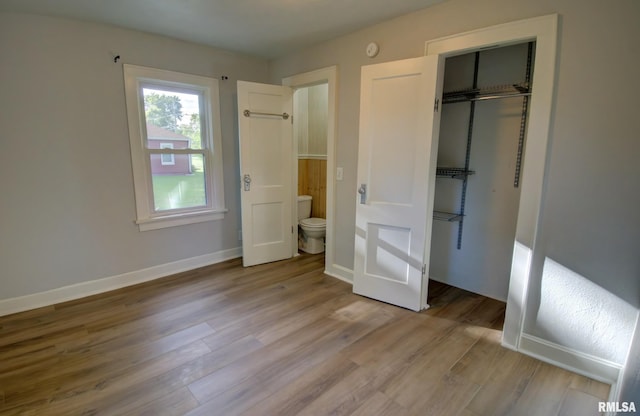 unfurnished bedroom with ensuite bath, light wood-type flooring, and a closet