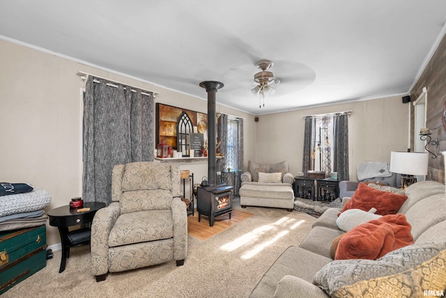 living room featuring ceiling fan, light colored carpet, a wood stove, and crown molding