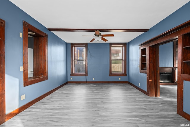 empty room with ceiling fan, beamed ceiling, and wood-type flooring