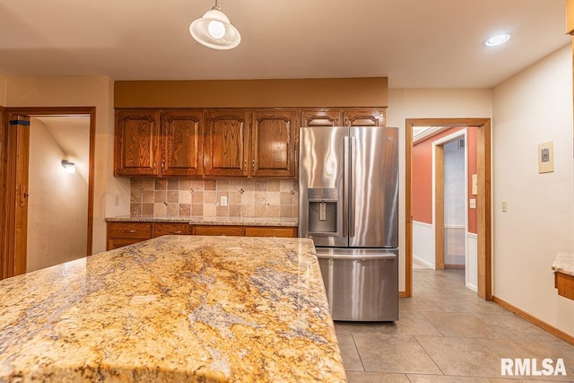 kitchen with stainless steel fridge, tasteful backsplash, decorative light fixtures, light tile patterned flooring, and light stone countertops